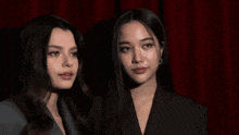 two women standing next to each other with a red curtain in the background
