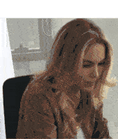 a woman in a brown jacket is sitting in a chair in front of a window