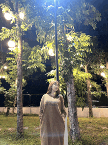 a woman in a brown dress with the word brooklyn on it stands in front of trees