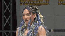 a woman with blue hair stands in front of a wall that says marigold
