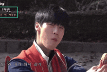 a young man in a red jacket is holding a piece of food in his hand
