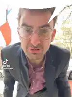 a man wearing glasses and a suit has tiktok written on the bottom right
