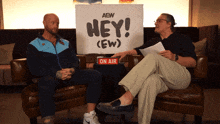 two men sit on a couch with a sign that says hey