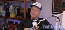 a man wearing a baseball cap is sitting in front of a microphone in a dark room .