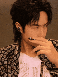 a man covering his mouth with his hand while wearing earrings and a watch