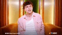 a man in a pink shirt is sitting in a chair with the nbc logo on the bottom right