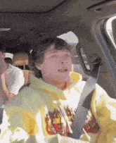 a young man wearing a yellow hoodie with flames on it sits in a car