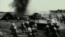 a black and white photo of soldiers running in front of a tank .