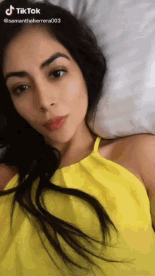 a woman in a yellow top is laying on a bed and has a tiktok account