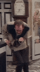 a man in a sweater is standing in front of a grandfather clock and a woman behind him