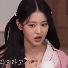 a girl in a pink shirt is holding a bowl of food with chopsticks .