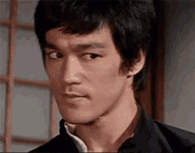 bruce lee is making a funny face while looking at the camera in a room .