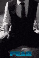 a man in a suit and tie is sitting on a bed with the word fear written in blue