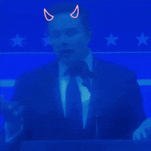 a man in a suit and tie stands in front of a microphone with neon devil horns on his head