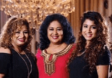 three women are standing next to each other in front of a chandelier and smiling .