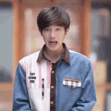 a young man wearing a denim jacket and a plaid shirt is making a face .