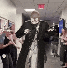 a man in a suit and tie is dancing in a hallway with an exit sign above him