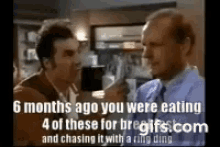 two men are standing next to each other in a kitchen talking to each other .