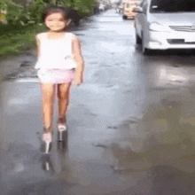 a little girl is riding a scooter on a wet road .
