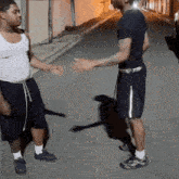 a man in a white tank top and black shorts is standing next to another man in black shorts