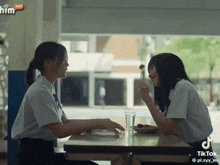 two girls are sitting at a table and one is holding a spoon