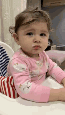a baby girl in a pink outfit is sitting in a high chair with a messy face .