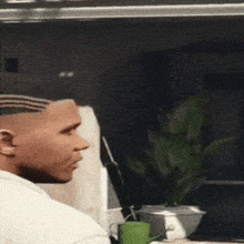 a man with a shaved head sits at a table with a green cup