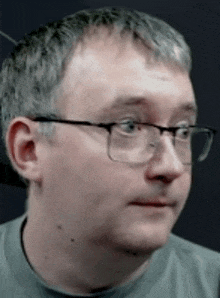 a man wearing glasses and a grey shirt is making a funny face .