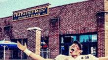 a man with his arms outstretched in front of a brick building that says ' innistery ' on it