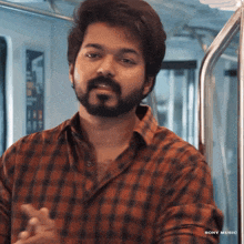 a man with a beard wearing a plaid shirt with the word sony music on the bottom