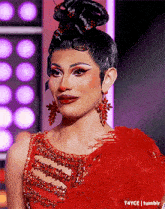 a drag queen is wearing a red dress and red earrings .