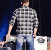 a man in a plaid shirt is standing in front of an amp