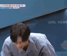 a man in a striped shirt is laughing while sitting in front of a blackboard .