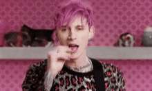 a man with pink hair and a leopard print jacket is eating a lollipop .