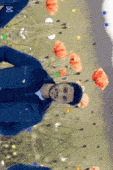 a man in a blue jacket stands in a field of flowers with a reflection of himself in the flowers
