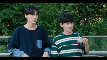 two young men standing next to each other with one holding a cup of soda
