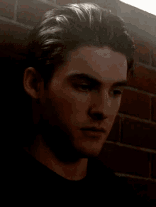 a man in a black shirt is standing in front of a brick wall