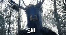 a man with a beard and antlers is standing in the woods with the word sni written on the bottom .