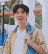 a young man wearing a yellow shirt and a white shirt is smiling and holding a blue backpack .