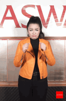 a woman in an orange jacket is making a funny face in front of a sign that says asw