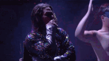 a man in a sequined jacket is singing on stage