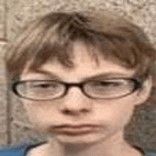 a young boy wearing glasses is looking at the camera .