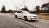 a white car with gold wheels is driving down the road