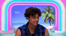 a man in a blue plaid shirt is sitting in front of a window with the name nic written on it