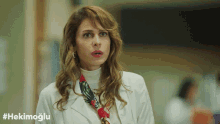 a woman in a white coat with a scarf around her neck and the hashtag #hekimoglu on the bottom