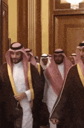 a group of men in traditional arabic clothing are walking in a room