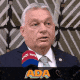 a man in a suit and tie is speaking into a microphone with the word ada written below him