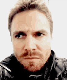 a man with a beard and a black jacket makes a face