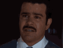 a man with a mustache is crying with his eyes closed and his mouth open .