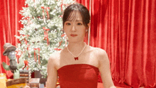 a woman in a red strapless dress is standing in front of a christmas tree .